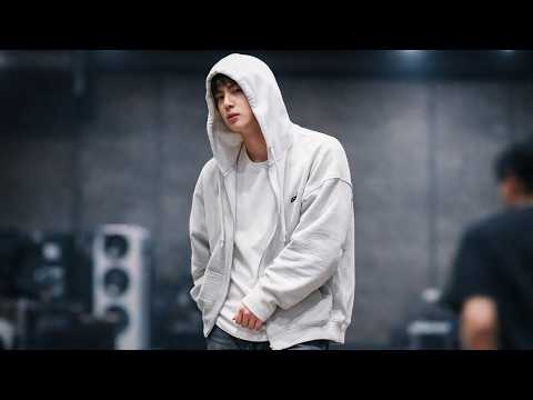 BTS Jin smiling and waving at fans during a performance or promotional event, possibly related to a fan voting achievement.
