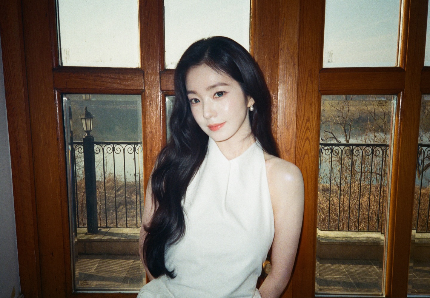 Irene from Red Velvet, wearing a white top and looking over her shoulder, on a dark background.
